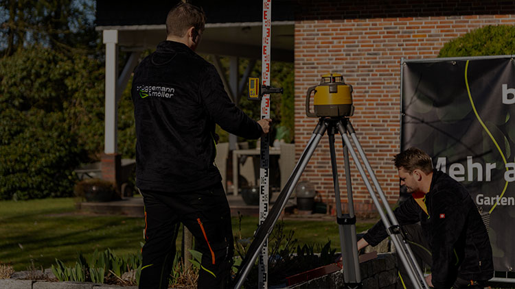 Mann hockt vor einer Mauer und hält eine Wasserwaage an
